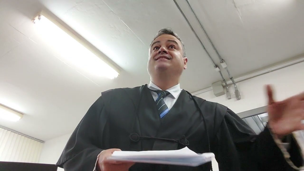 Quadro do v&iacute;deo: advogado de toga em p&eacute;, falando ao Conselho de Sentença no plen&aacute;rio do J&uacute;ri